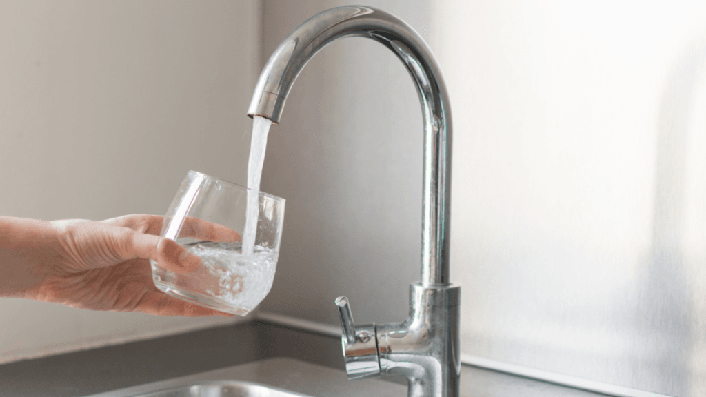 How Often Should You Service Your Home Filtration System? Hand holding a glass under a faucet, showing the results after you service your home filtration system.