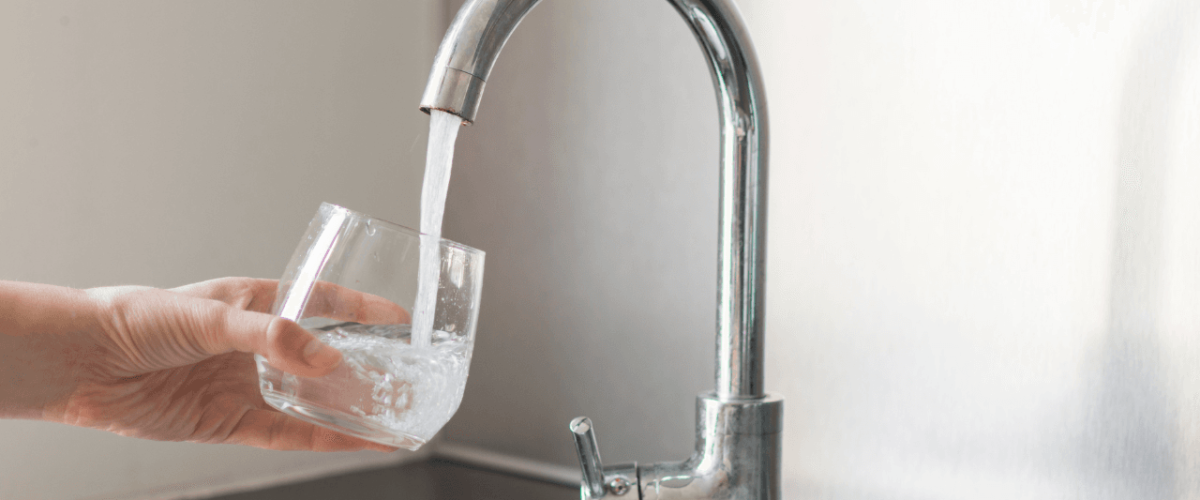 Hand holding a glass under a faucet, showing the results after you service your home filtration system.