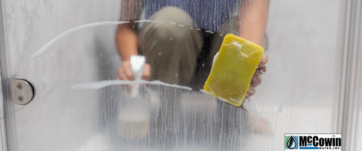 Scrubbing hard water stains off a shower door in Irvine, CA. McCowin Water provides local water hardness testing and whole-house filtration solutions.