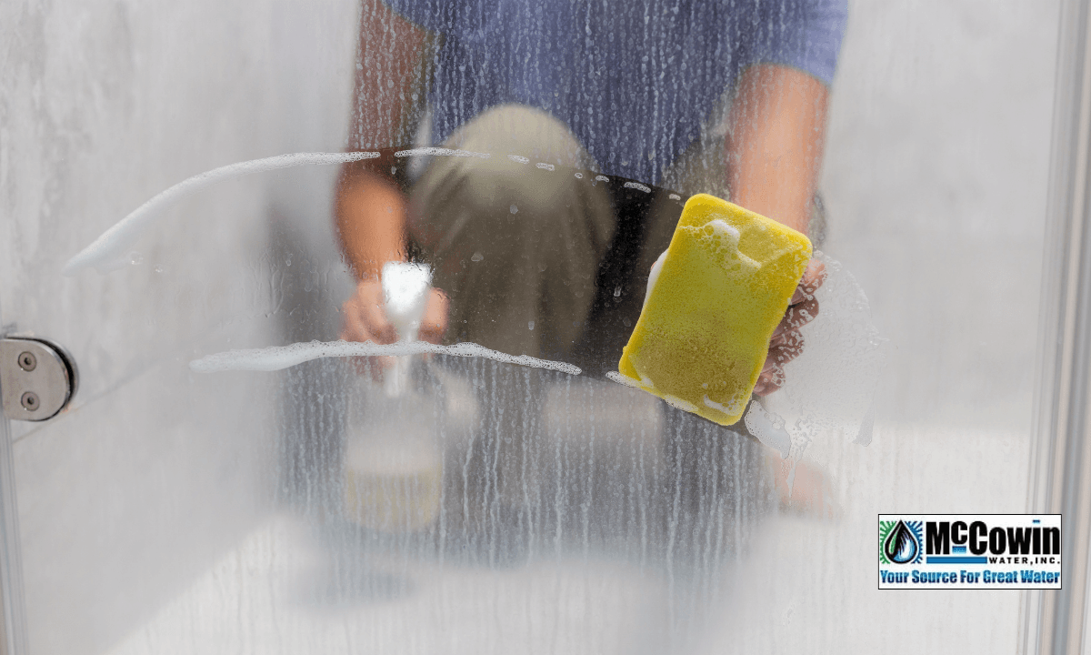 Scrubbing hard water stains off a shower door in Irvine, CA. McCowin Water provides local water hardness testing and whole-house filtration solutions.